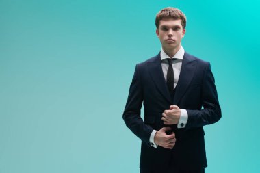 Kol düğmeleri ve şık bir takım elbiseyle klasik beyaz gömlekle poz veren yakışıklı, bakımlı bir genç. Açık mavi arka planda fotokopi alanı olan bir stüdyo. Erkek modası ve güzelliği. Klasik biçim.