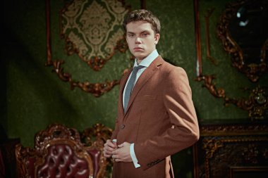 Pahalı takım elbiseli saygıdeğer bir genç adam zengin bir dairede klasik bir iç mimarisi ile duruyor. Erkek modası, lüks tarzı..