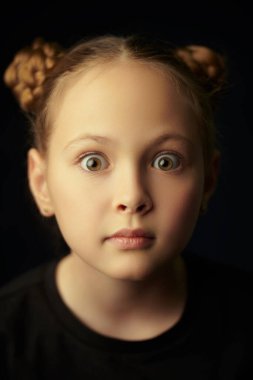 Kameraya şaşkınlıkla bakan güzel bir kızın stüdyo portresi. Çocuk duyguları. Mutlu çocuk konsepti. Siyah arkaplan.