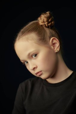 Siyah bir stüdyo arka planında siyah tişörtlü tatlı düşünceli bir kızın portresi. Çocuklar, duygular. Psikolojik resim.