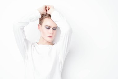 Erkek güzelliği ve moda. Yakışıklı, şehvetli, genç bir manken. Sarı saçlı, siyah dumanlı gözlü, beyaz duvarda poz veren. Uzayı kopyala Erkekler için güzellik kozmetiği. Makyaj ve saç stili.