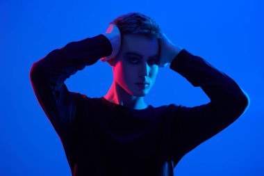 Stüdyoda karışık renkli neon ışıkta mavi arka planda poz veren seksi genç bir adamın sanat portresi. Erkek güzeli. Sanat Moda Konsepti. 