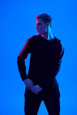 Stüdyoda karışık renkli neon ışıkta mavi arka planda poz veren seksi genç bir adamın sanat portresi. Erkek güzeli. Sanat Moda Konsepti. 