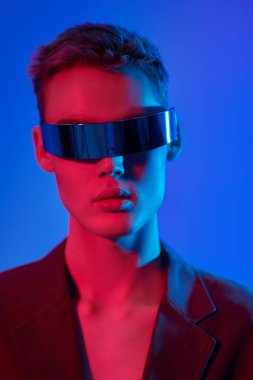 Gözlük stili. Mis mavisi ve kıpkırmızı ışıkta aynalı fütürist gözlüklerle poz veren şık bir gencin portresi. Mavi stüdyo geçmişi. Moda konsepti. 