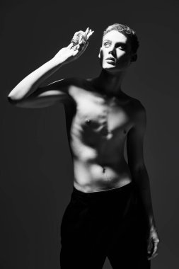 Seksi, genç bir mankenin çıplak bedeniyle çiçekle poz verirken çekilmiş siyah beyaz bir resmi. Siyah stüdyo geçmişi. Erkek güzelliği ve moda. Makyaj, saç stili ve makyaj malzemeleri..