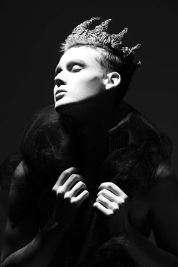 Çıplak Kral. Siyah beyaz bir resim. Yakışıklı bir genç çıplak vücut ve siyah stüdyo arka planında bir taç ile poz veriyor. Sanat ve Moda.