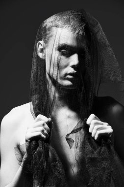 Sanat ve moda. Kafasını siyah örgü kumaşla örten genç bir adamın portresi. Gri stüdyo geçmişi. Erkek güzelliği ve moda. 