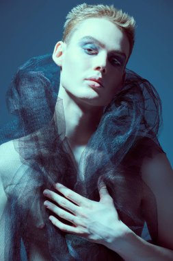 Siyah örgü kumaşlı çıplak gövdeli şehvetli genç bir mankenin sanat portresi. Gri stüdyo geçmişi. Erkek güzelliği ve moda. Makyaj, saç stili ve makyaj malzemeleri..