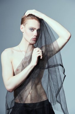 Sanat ve moda. Kafasını siyah örgü kumaşla örten genç bir adamın portresi. Gri stüdyo geçmişi. Erkek güzelliği ve moda. 