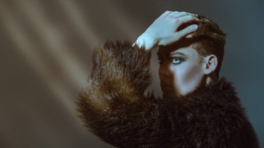 Kısa saç kesimi ve siyah dumanlı gözleriyle stüdyoda siyah kürklü poz veren şık bir gencin portresi. Moda ve erkek güzelliği. Makyaj ve saç stili, kozmetik..