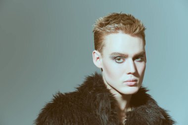 Kısa saç kesimi ve siyah dumanlı gözleriyle stüdyoda siyah kürklü poz veren şık bir gencin portresi. Moda ve erkek güzelliği. Makyaj ve saç stili, kozmetik..