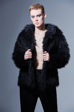 Kısa saç kesimi ve siyah dumanlı gözleriyle stüdyoda siyah kürklü poz veren şık bir gencin portresi. Makyaj, saç stili, makyaj malzemeleri. Moda ve erkek güzelliği. 