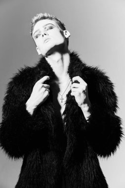 Kısa saç kesimi ve siyah dumanlı gözleriyle stüdyoda siyah kürklü poz veren şık bir gencin portresi. Makyaj, saç stili, makyaj malzemeleri. Moda ve erkek güzelliği. 