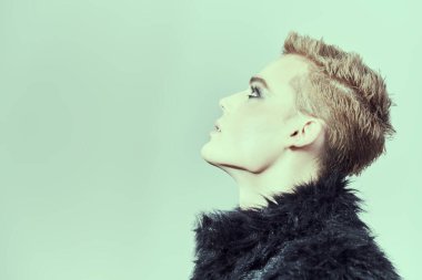 Kısa saçlı, siyah dumanlı gözlü, siyah kürklü bir gencin profil portresi. Moda ve erkek güzelliği. Makyaj, saç stili, makyaj malzemeleri. Boşluğu kopyala.