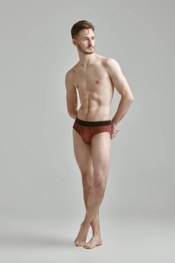 Beyaz bir stüdyo arka planına çıplak poz veren yakışıklı bir sporcunun tam boy portresi. İç çamaşırı ve erkek güzelliği..