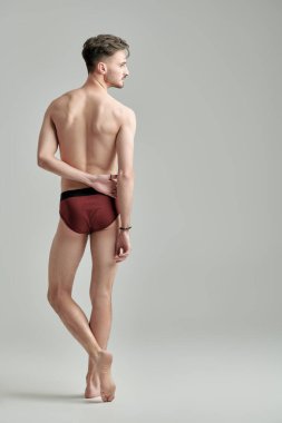 Beyaz bir stüdyo arka planında erkek donu içinde çıplak poz veren yakışıklı bir atletin tam boy arka portresi. İç çamaşırı ve erkek güzelliği..