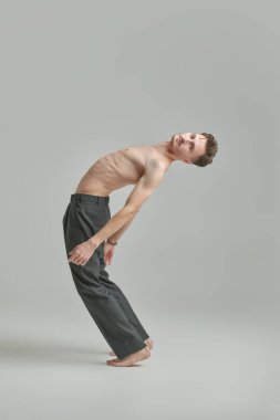 Gri stüdyo arka planında çıplak gövdesi olan yakışıklı esmer bir adamın tam boy portresi. Erkek sağlığı ve güzelliği.