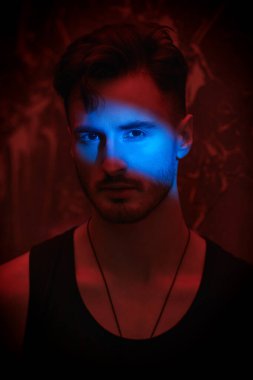 Bir adamın sanat portresi. Atletik yapılı vahşi esmer bir adam kırmızı ışıklı karanlık bir odada duruyor. Yüzüne mavi bir ışık hüzmesi düşer. Erkek güzelliği, erkeklik. Duygular.