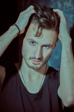 Erkeklik ve erkek güzelliği. Siyah bir kolsuz bluzla beton duvara karşı poz veren yakışıklı, esmer bir adamın portresi..