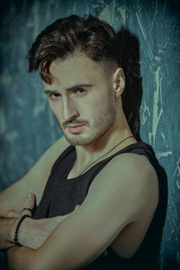 Beton duvara karşı siyah bir kolsuz bluzla poz veren yakışıklı, esmer bir adamın portresi. Erkeklik ve erkek güzelliği. 