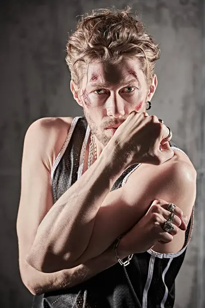 Yüzünde çizikler ve yaralar olan, beton duvarların önünde kameraya bakan vahşi bir adamın portresi. Aksiyon filmi kahramanı. Dedektif filmi. Kötü adam..