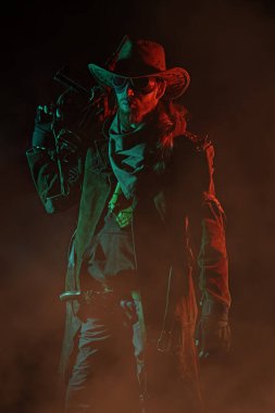 Deri ceketli, kovboy şapkalı ve gözlüklü öfkeli bir adam kırmızı ve yeşil ışıkta duran bir tüfekle ateş ediyor. Kıyameti haber veren kovboy.. 