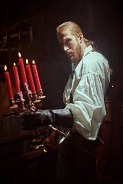 Bir silahşör asilzade gece kalede elinde mumlarla dikiliyor. Tarihi bir romanın kahramanı. 16.-17. yüzyılın tarihi yeniden yapılandırması.. 