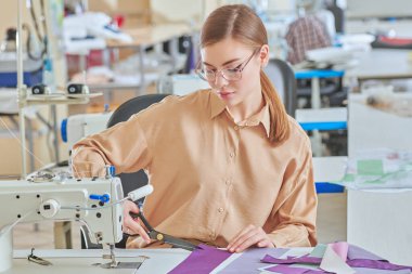 Dikiş atölyesi. Genç, güzel bir terzi dikiş makinesinde çalışıyor. Moda endüstrisi. Moda tasarımcısı.