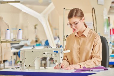 Mutlu yaratıcı genç bir terzi kız atölyede yeni bir ürün dikiyor. Moda endüstrisi. Giysi imalatı.