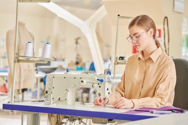 Giysi imalatı. Mutlu yaratıcı genç bir terzi kız atölyede yeni bir ürün dikiyor. Moda endüstrisi. 