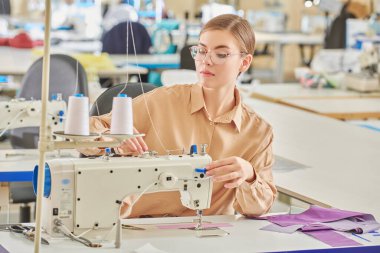 Mutlu yaratıcı genç bir terzi kız atölyede yeni bir ürün dikiyor. Moda endüstrisi. Giysi imalatı.