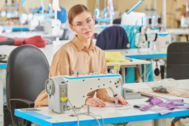 Giysi imalatı. Güzel bir genç kız terzi dikiş atölyesinde yeni bir ürün dikiyor. Moda endüstrisi.