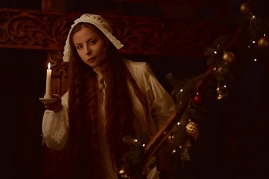 Gecelik ve kepli güzel aristokrat bayan geceleri bir mum ile zengin bir iç mekanda duruyor. 19. yüzyıl - 20. yüzyıl başlarındaki romanın kahramanı. Klasik stil.