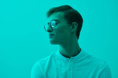 Beyaz gömlekli ve şık gözlüklü zarif sarışın bir adam. Başarılı bir insan. İş adamı. Turkuaz bir arka planda karışık ışıkla stüdyo çekimi. Gözlük modası. Boşluğu kopyala.