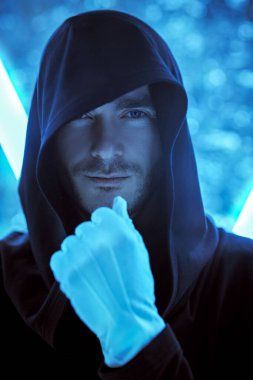 Fantezi kahramanı. Siyah bir bornoz giymiş, kafasında bir başlıkla neon lambaların ışığında duran cesur görünümlü yakışıklı bir adamın yakın çekimi. Uzay hakkında bilim kurgu. Sanal tema.