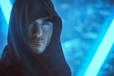 Kafasında bir başlık olan siyah bir bornoz giymiş cesur bakışlı vahşi bir adam neon lambaların ışığında duruyor. Fantezi kahramanı. Uzay ve gelecek dünya hakkında bilim kurgu. Sanal tema.