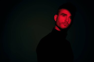 Karanlık bir arka planda gölgede duran ve düşünceli bir şekilde ileriye bakan bir adamın portresi. Gözleri bir kırmızı ışık demeti tarafından aydınlatılır. Uzayı kopyala Psikolojik sanat portresi.