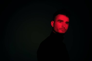 Karanlık bir arka planda gölgede duran ve düşünceli bir şekilde ileriye bakan bir adamın portresi. Gözleri bir kırmızı ışık demeti tarafından aydınlatılır. Uzayı kopyala Psikolojik sanat portresi.