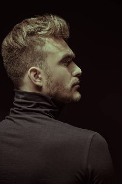 Siyah takım elbiseli yakışıklı bir adamın profil portresi. Yan tarafa bakıyor. Stüdyo siyah arkaplanı. 