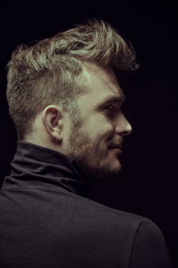 Siyah takım elbiseli yakışıklı bir adamın profil portresi. Yan tarafa bakıyor. Stüdyo siyah arkaplanı. 