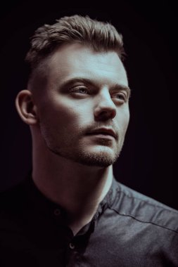 Siyah takım elbiseli yakışıklı bir adamın portresi. Yan tarafa bakıyor. Stüdyo siyah arka plan. Psikolojik resim.