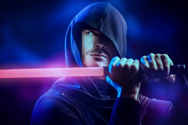 Uzay fantezisi. Bilim kurgu romanı. Siyah cüppeli, kapüşonlu cesur bir savaşçı karanlık bir arka planda lazer kılıcı tutuyor..