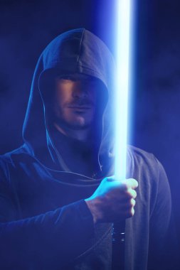 Kafasında kapüşonlu siyah cüppesi olan cesur bir savaşçı karanlık uzayın arka planına karşı önünde bir lazer kılıcı tutuyor. Uzay fantezisi. Bilim kurgu romanı.