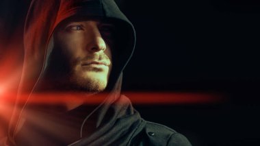 Yüzü siyah bir kaputun altına gizlenmiş, sert görünüşlü bir adamın yakın plan portresi. Psikolojik sanat portresi. Karışık ışık.