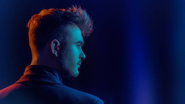 Sırtını dönüp yan tarafa bakan yakışıklı, vahşi bir adamın portresi. Karma ışık ve kopyalama alanı olan siyah bir stüdyo. Psikolojik sanat portresi.