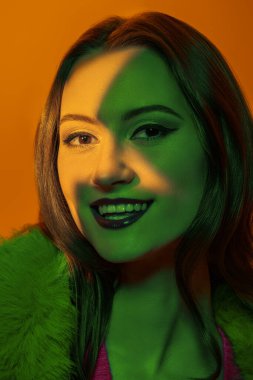 Yeşil ışıklandırmalı sarı arka planda zarif makyajlı güzel esmer bir kadının yakın plan portresi. Stüdyo çekimi. Makyaj ve kozmetik. 
