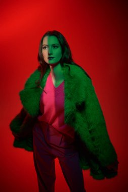 Parlak fuşya kıyafetleri içinde şık zarif bir kadın ve karışık renklerde kırmızı arka planda yeşil kürklü bir kadın. Parlak renkler, tarz ve moda. Stüdyo çekimi.