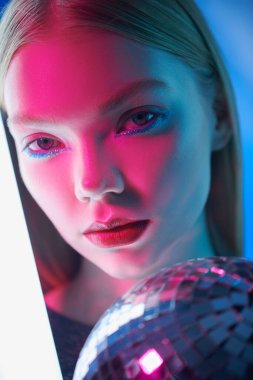 Parlak makyajlı güzel bir sarışın kız parlak bir disko topuyla neon ışığında poz veriyor. Güzellik ve makyaj. Göz kamaştırıcı parlak stil, sanatsal makyaj. Disko, gece kulübü..