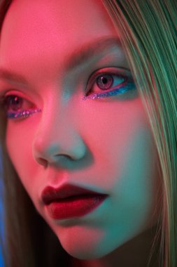 Güzellik konsepti, makyaj ve makyaj malzemeleri. Parlak makyajlı, neon mavisi kıpkırmızı bir kızın yakın plan portresi. Göz kamaştırıcı bir stil..