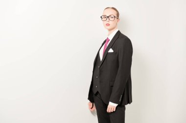 İş stili. Güzel bir kızın stüdyo portresi. Katı makyaj ve saç stili. Zarif siyah bir takım elbise ve beyaz arka planda şık gözlük takıyor. Moda fotoğrafı. Boşluğu kopyala.